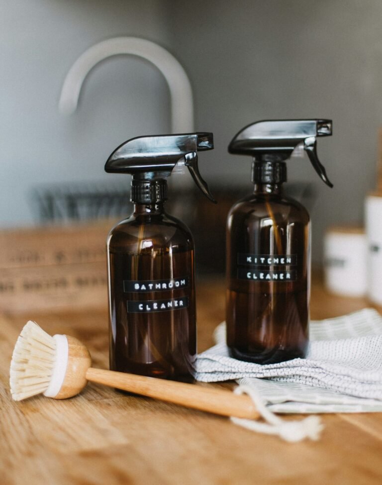 Amber glass spray bottles labeled bathroom cleaner and kitchen cleaner representing cleaning product certifications on a wooden counter.