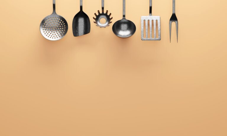 pexels dada design 240566386 12292638 Six best stainless steel cooking utensils arranged on a peach background, including spoons, a ladle, slotted turner, pasta server, and carving fork.